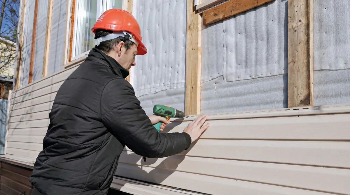 Siding replacement professional using a power drill to install new tan vinyl siding on a home exterior in Oakland, CA